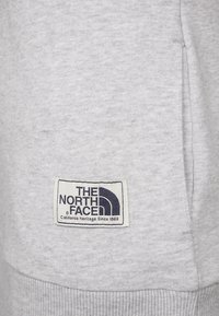 Tissu gris clair avec une étiquette rectangulaire "The North Face" en texte et logo noirs, indiquant "California Heritage Since 1968".