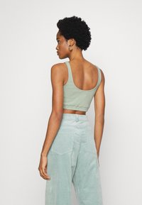 Top de alças largas, verde-claro, cortado, com bainha elástica, combinado com calças de veludo cotelê verde-claro, texturizadas e de cintura alta.