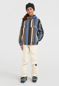 Sudadera con capucha colorida con rayas en forma de chevron en azul, negro y marrón, combinada con pantalones de nieve en blanco roto y botas de esquí grises.