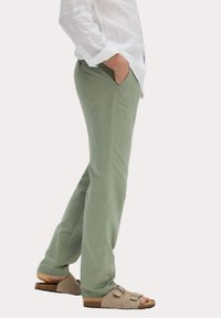 Pantalons en coton léger de couleur olive avec une coupe droite, poches latérales et une texture lisse, associés à des sandales beiges avec des brides réglables.