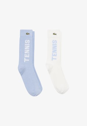 Coppia di calzini al ginocchio, uno azzurro chiaro e uno bianco, ciascuno con testo "TENNIS" e piccolo logo verde del coccodrillo vicino alla parte superiore.
