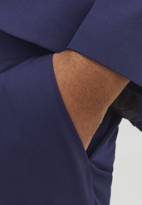Mørkeblå topp med glatt, elastisk stoff og sidelomme. Nærbilde viser detaljene på ermet og teksturene.