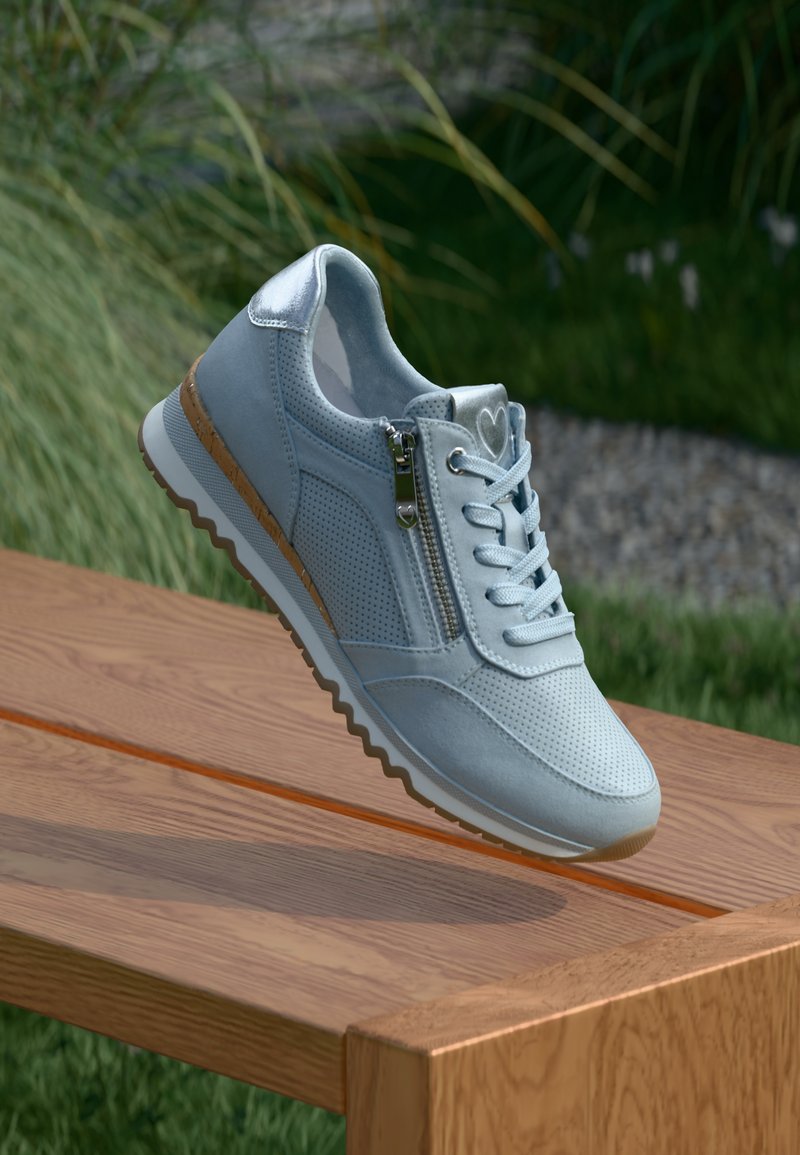 Svijetloplave tenisice s perforiranim dizajnom, srebrnim naglascima i bočnim patentnim zatvaračem. Teksturirana potplat s detaljem u obliku plute smeđe boje duž ruba.