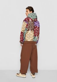 Hooded jacket with a multicolored patchwork design in red, green, purple, and beige. Brown wide-leg pants with a casual fit and pockets.