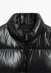 Giacca a vento nera con collo alto, finitura lucida e chiusura frontale con cerniera. Caratterizzata da una texture trapuntata e un'imbottitura leggera.