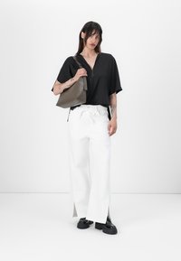 Haut noir à manches courtes avec fermeture éclair, associé à un pantalon large blanc avec des fentes. Un sac à épaule gris et des chaussures à plateformes noires imposantes.