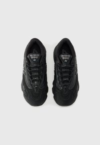 Juodi sportiniai batai su tinklinėmis detalėmis, tekstūruotais sintetiniais akcentais, apvaliu pirštu ir paminkštintu padu. Yra „New Balance 1000“ ženklas.