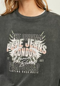 Sudadera gris oscuro con un estampado gráfico vintage con acentos en blanco y tonos pastel. El diseño incluye texto y elementos decorativos.