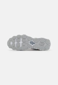 Suela de una zapatilla Nike con empuñaduras redondas texturizadas, un emblema central de la marca Nike y el logo NIKE sobre un fondo blanco.