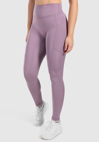 Leggings violets taille haute en tissu extensible, avec des poches latérales et des détails de surpiqûre subtils. Assortis avec des chaussures de sport blanches.