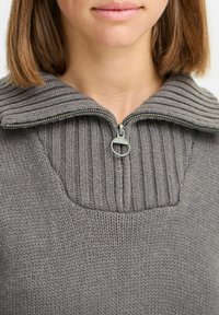 Grå stickad tröja med ribbad krage och halvdragkedja, med en texturerad kropp och en slät stickad finish på ärmarna.