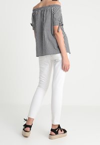 Black and white checked off-the-shoulder top with tied sleeves, paired with white fitted jeans and black espadrille sandals.