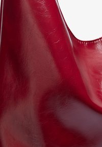 Sac en cuir rouge avec une surface lisse et brillante ; présente une ouverture arrondie et des variations de texture subtiles. Design léger et flexible.