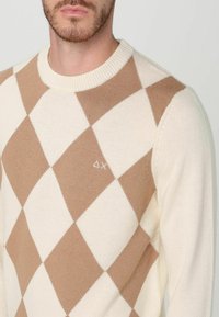 Maglione cream con motivo a diamante in marrone chiaro, con scollo a costine e piccolo logo sul petto. Texture in maglia morbida.