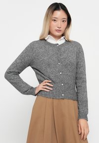 Grijze gebreide cardigan met een ronde halslijn, lange mouwen en vijf doorzichtige knoopsluitingen aan de voorkant. Lichtjes verkorte zoom.