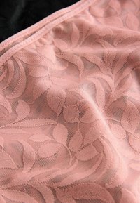 Rosa Spitze mit floralem Muster, das eine strukturierte Oberfläche aufweist. Das Material ist weich und durchsichtig, mit einem kontrastierenden schwarzen Rand.
