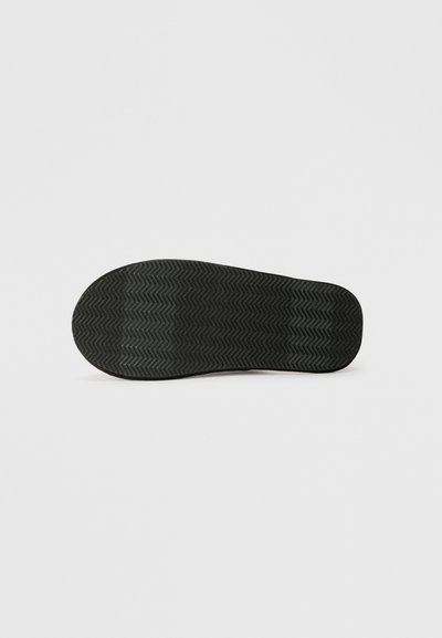 Suela de zapato negra con un dibujo de zigzag, mostrada en posición horizontal sobre un fondo claro y liso.