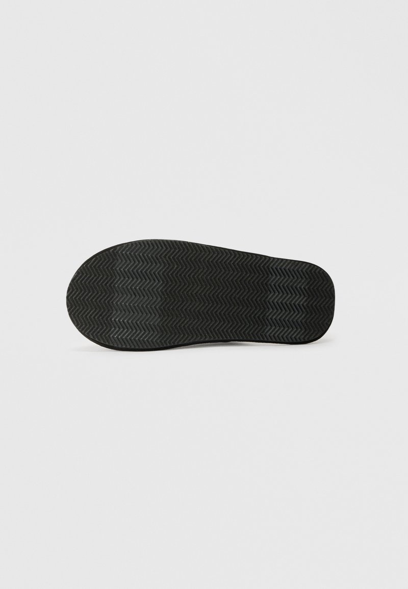 Schwarze Schuhsohle mit einem zickzackförmigen Profil, flach auf einem schlichten hellen Hintergrund dargestellt.