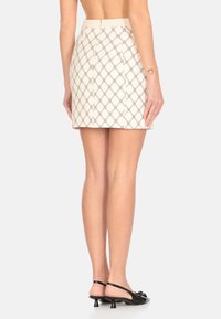 Gonna mini color crema con un motivo a rombi neri, design aderente, texture liscia e chiusura con cerniera sul retro. Abbinata a scarpe slingback nere con tacco.