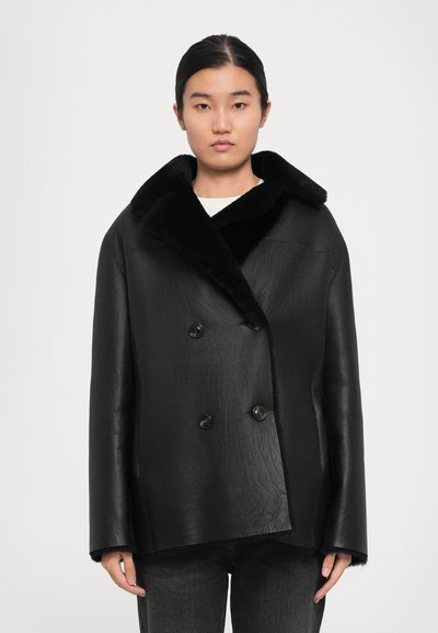 Schwarze Lederjacke mit doppelter Knopfreihe, großem Fellkragen, strukturiertem Finish und braunen Knopfdetails. Kurze Länge und gerade Passform.