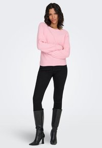 Maglione rosa chiaro a coste con scollo ampio, abbinato a jeans aderenti neri e stivali neri sopra il ginocchio con tacco.