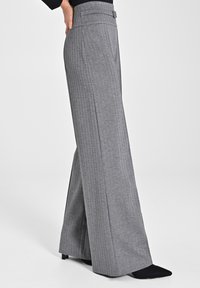 Pantaloni a gamba larga in un motivo a quadri grigi, realizzati in un tessuto liscio. Presentano una vita alta con passanti per cintura e dettagli di piega sartoriale.