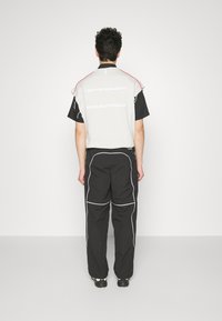 Harmaa ja musta lyhythihainen paita, jossa teksti "REDEFINED", yhdistetty mustiin housuihin, joissa on valkoiset pipotukset ja rento istuvuus.