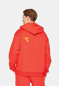 Felpa rossa in misto cotone con vestibilità comoda. Presenta un logo giallo sul retro e una tasca a marsupio. Texture liscia con polsini a costine.