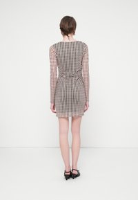 Rochie lungă din material transparent cu un model în carouri maro și bej, siluetă ajustată și tiv curbat, purtată cu pantofi cu toc negri.