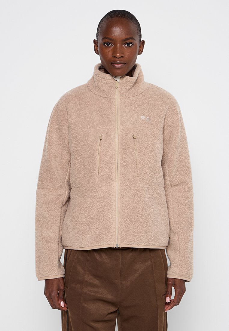 Beige Fleece-Jacke mit hohem Kragen, durchgehendem Reißverschluss und zwei Reißverschlusstaschen auf der Brust. Weicher Stoff, lockere Passform und leicht verkürzte Länge.