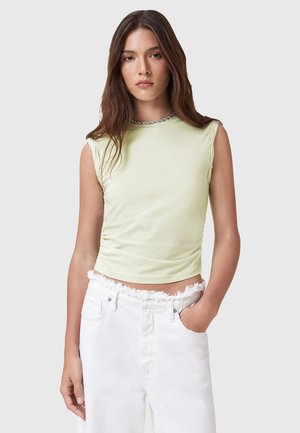 Top senza maniche fitted di un verde chiaro con un design arricciato e un collo rotondo rifinito in argento, abbinato a pantaloni corti in denim bianco con orlo sfrangiato.