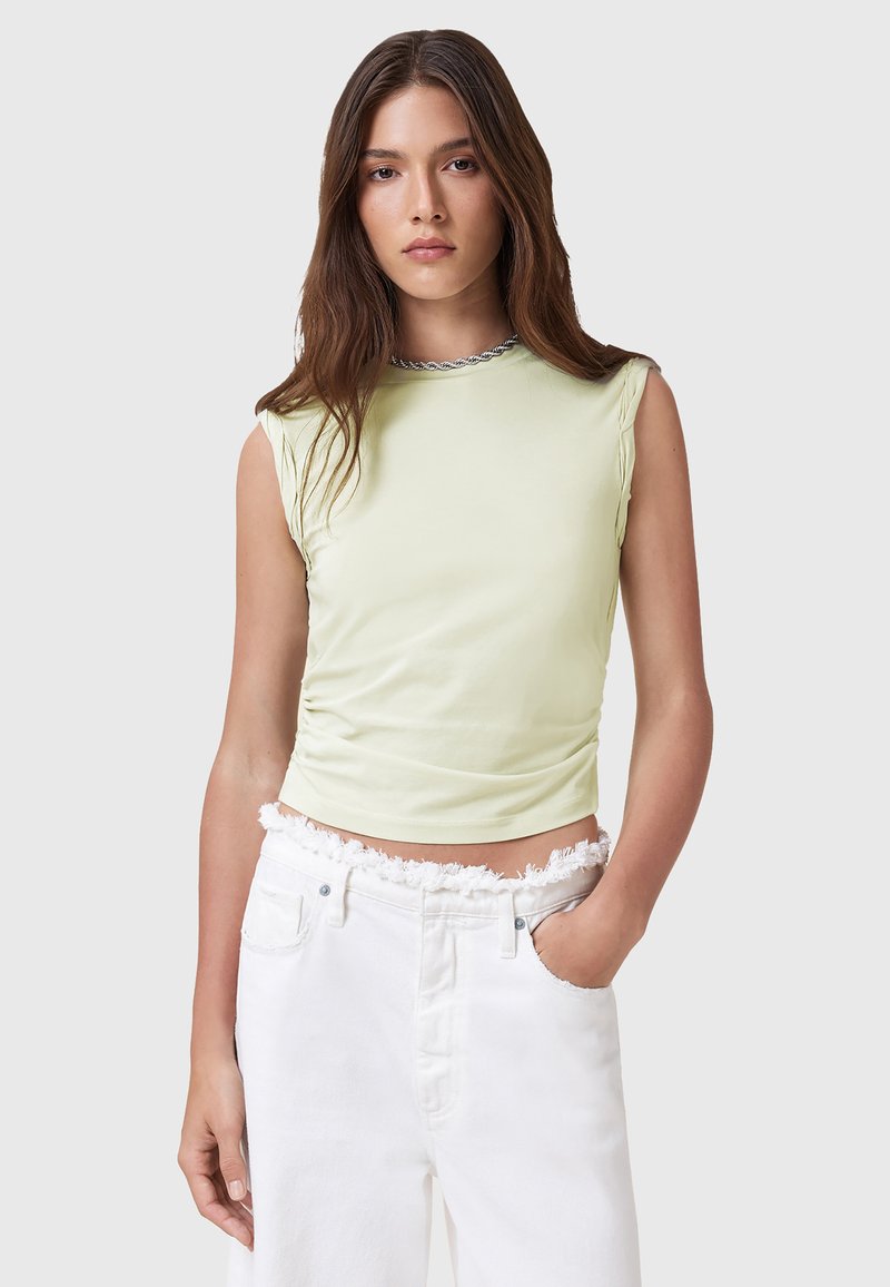 Top senza maniche fitted di un verde chiaro con un design arricciato e un collo rotondo rifinito in argento, abbinato a pantaloni corti in denim bianco con orlo sfrangiato.
