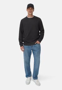 Zwart sweatshirt met een ronde halslijn, gecombineerd met vervaagde blauwe rechte jeans en witte sneakers. Een zwarte pet met een logo maakt de look compleet.