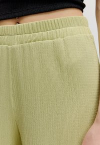 Hellgrüne, strukturierte Hose aus geripptem Material, mit einem elastischen Bund und subtilen Steppnähten. Nahaufnahme des Materials und der Passform.