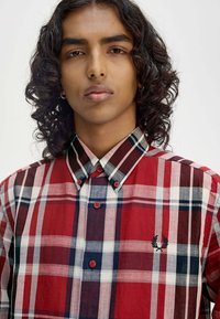 Rood en marineblauw geruite shirt met een button-down kraag, voorzien van contrasterende witte en donkerblauwe strepen, en een klein logo op de borst.