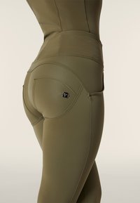 Leggings verde oliva realizzati in materiale liscio ed elastico, con un design a cuciture curve e un piccolo etichetta con il marchio sul retro.