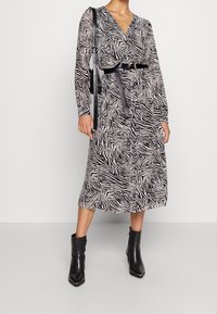 Vestido cruzado de manga larga en estampado de cebra negro y crema, ceñido a la cintura con un cinturón, combinado con botines negros. Tejido suave, de longitud midi.