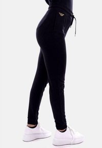 Zwarte joggerbroeken met een trekkoord in de taille, slim fit en een logo met gouden accent op de zak. Gecombineerd met witte platform sneakers.