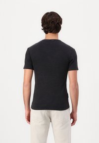 Sort kortærmet t-shirt, rund halsudskæring, let struktureret stof, set bagfra. Samlet med lyse, lige ben bukser.