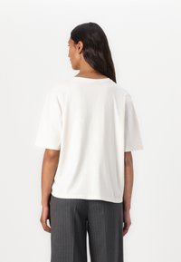 White cotton t-shirt with a relaxed fit, short sleeves, and a round neckline, shown from the back, paired with gray pinstriped trousers.