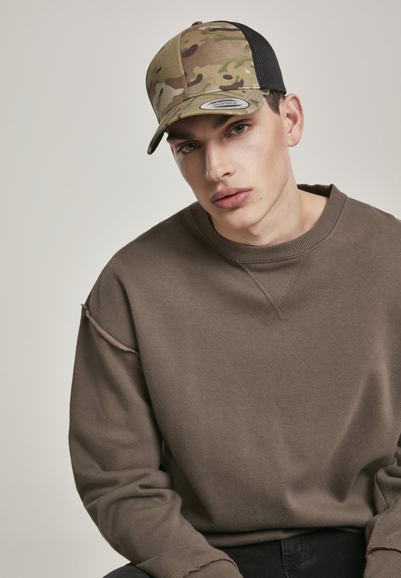 Vrachtwagenchauffeur pet met een camouflage ontwerp en een zwarte gaas achterkant. Model draagt een bruine sweatshirt met een gestikt detail op de mouw.