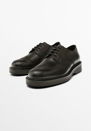 Black leather shoes with a classic derby design, featuring perforated detailing, rounded toe, and a thick rubber sole.
