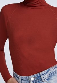 Maglione a collo alto color ruggine con texture a costine e maniche lunghe, abbinato a pantaloni shorts in denim a vita alta di colore blu chiaro.