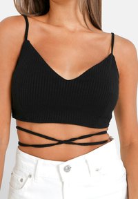 Crop top nero a costine con scollo a V e spalline sottili. Presenta dettagli incrociati in vita, in contrasto con pantaloni corti bianchi a vita alta.