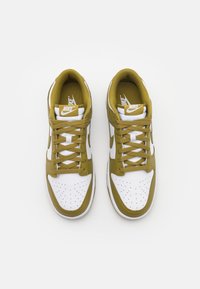 Nike tenisky v olivově zelené a bílé barvě, s texturovanou kůží, perforovanou špičkou, kulatými tkaničkami a nízkým designem.