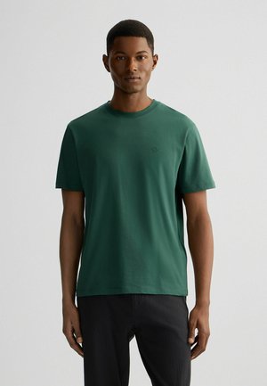Tricou verde din bumbac cu guler rotund și mâneci scurte, având un detaliu subtil al logo-ului pe piept și un design lejer.