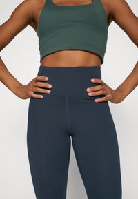 Mörk teal cropped topp och högmidjade marinblå leggings, båda gjorda av ett smidigt, stretchtåligt tyg, med synliga söms detaljer längs sömmarna.