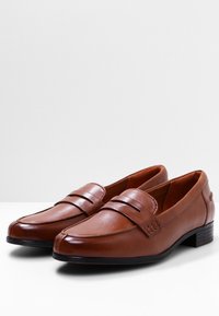 Mocassins en cuir marron à texture lisse, dotés de deux bandes horizontales et d'un talon bas empilé pour la stabilité.