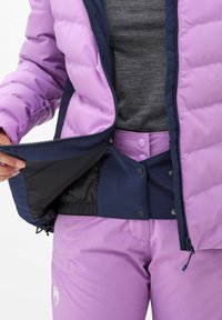 Hellblau gefütterte Jacke mit navyfarbenen Akzenten, ausgestattet mit einem Reißverschluss und einem schwarzen Innenfutter. Getragen mit passenden hellblauen Hosen.