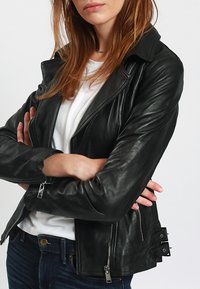 Giacca da moto in pelle nera con chiusura a zip frontale, colletto asimmetrico e accessori in metallo argentato. Presenta una vestibilità aderente e cuciture distintive.